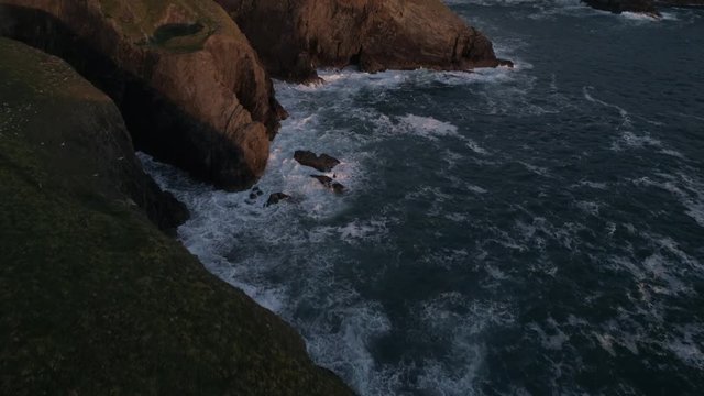Flying over the sea and cliffs with waves breaking against the rocks, English coast, Perranporth Beach