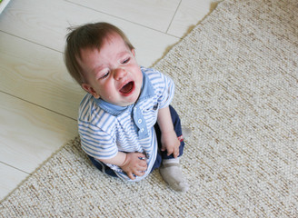 Little boy sitting on the floor, he's upset and crying. The child is crying sitting on the floor in the room..