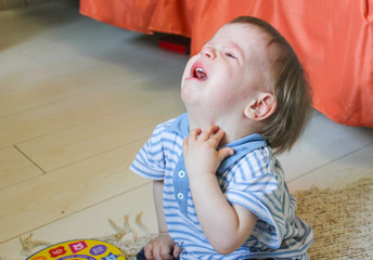 Little boy sitting on the floor, he's upset and crying. The child is crying sitting on the floor in the room..