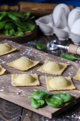 Not cooked ravioli on a wooden board, in the background a rolling pin and spinach and eggs