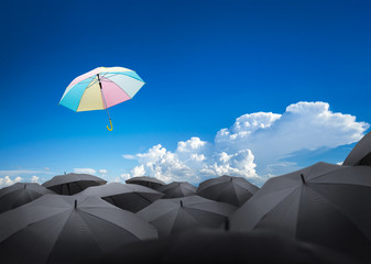 abstract umbrella flying over many black umbrellas with beautiful sky, leadership background...