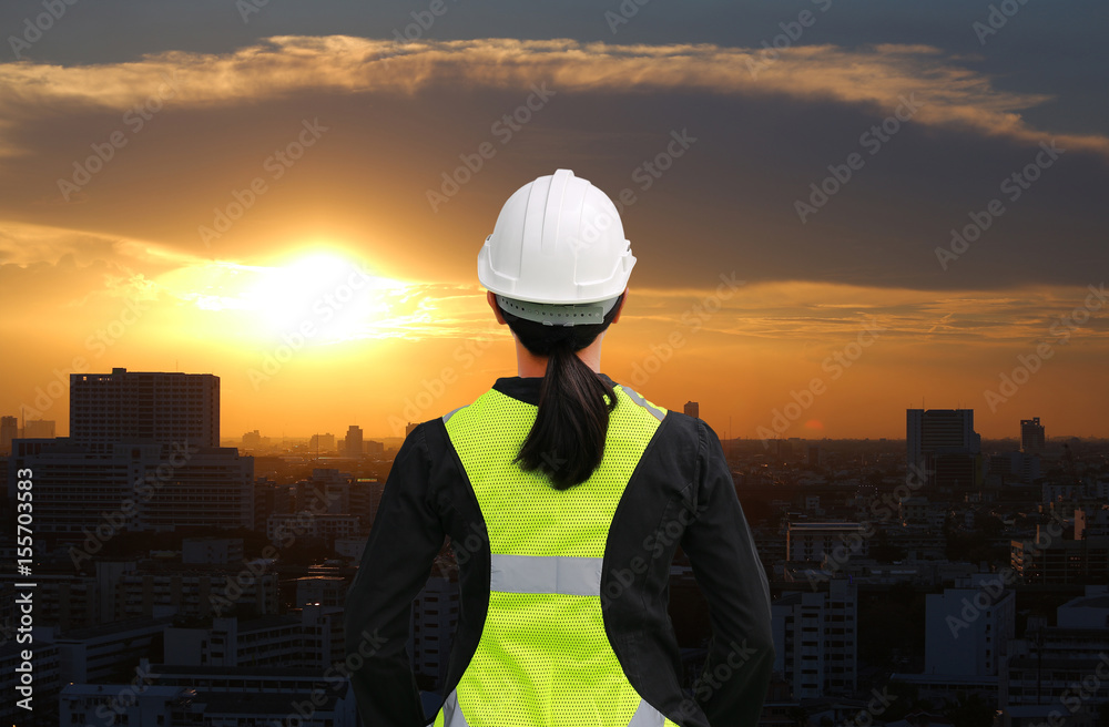 Wall mural back view of female construction worker against building at sunset in bangkok city background.