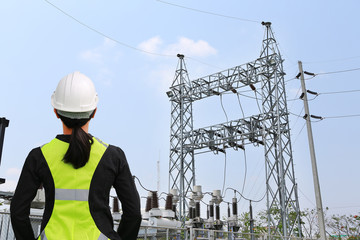 Back view of female construction worker against power plant background.
