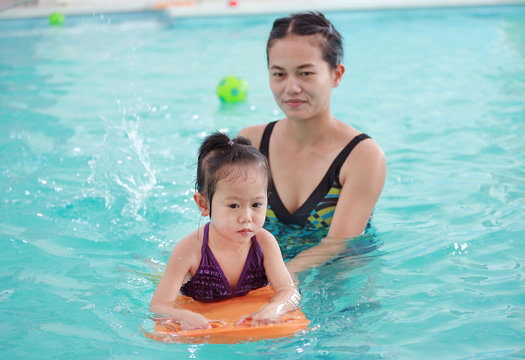 family of mother teaching kid in swimming pool.