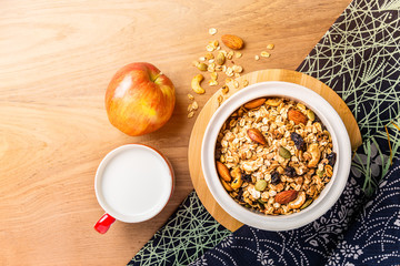 morning cereal in a bowl with full apple and cup of milk on wood table with asian style napkin