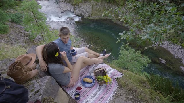 Woman Passes Her Boyfriend Some Orange Juice At A Picnic High Above A River