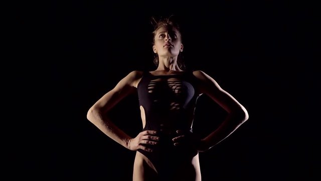 Young girl in black sexy lingerie is in a dark room under the light painting lamps