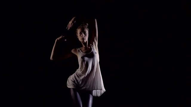 Athletic young girl doing exercises in the stretch in a dark room studios