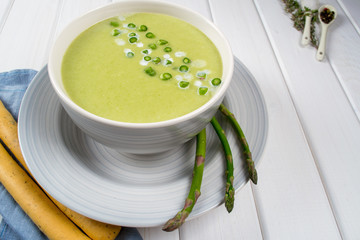 Green spring pureed cream asparagus soup in ceramic bowl on white wooden table