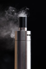 An electronic cigarette works on a black background and produces smoke