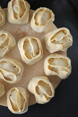Manti on a round  board isolated on a black background. Manti raw. Traditional meat dish
