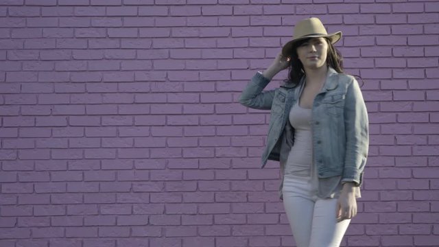 Young Woman With A Hat Poses In Front Of Pink Brick Wall