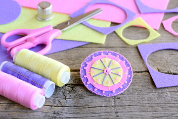 Obraz premium Felt circle flower decorated with beads. Handmade flower felt crafts, scissors, thread, colored felt sheets, thimble on vintage wooden background. Simple and quick felt crafts. Teaching kids to sew
