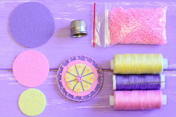 Obraz premium Felt flower, colored felt circles, thread spools, needle, thimble, pink beads on a wooden table. Sewing felt flower tutorial. Simple round felt flower crafts for kids. Top view