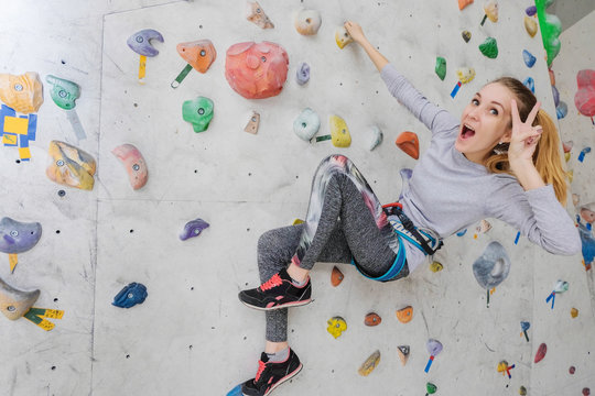 Woman climbing on climbing wall. The girl shows a victory gesture. Teenage rock climber.