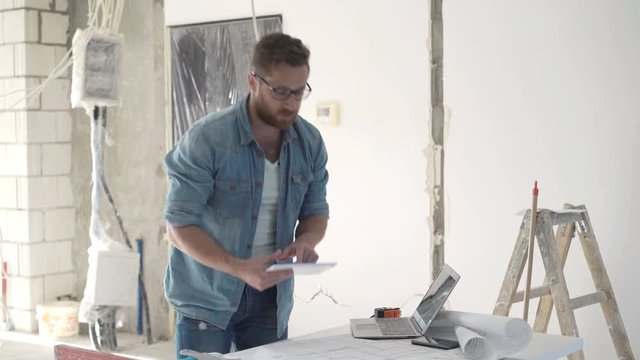 Man working with tablet and blueprints during renovation at new home
