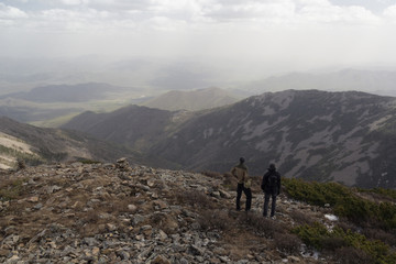 Fototapeta premium Two people stand side by side on top of the mountain and admire the mountain scenery