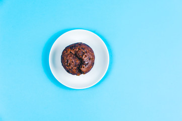 Tasty chocolate cupcake on plate on blue background. Top view. Space for text.