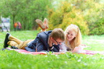 young attractive couple wearing glasses is working or studying with laptop book note and pen lying on blanket in green park at sunny day