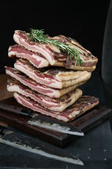 still life with sliced Italian jerked lunch meat, rosemary, cutting board and steel knife on a dark...