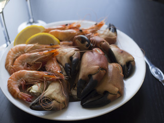 Boiled crab claws, whole prawns and slices of lemon on white plate with a wine glass in the background