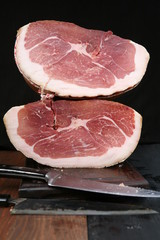 still life with the Italian meat proscutto for the  lunch, cutting board and steel knives on a dark background in close-up