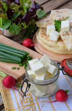 Square cubes of traditional greek cheese feta with flat bread, lettuce, onion and radish on wooden background.