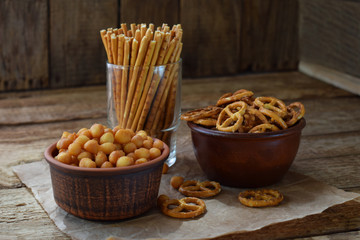 Salty snacks on wooden background. Crackers, pretzel, salted straws, nuts, dried fish. Junk food for beer or cola. Photographed with natural light