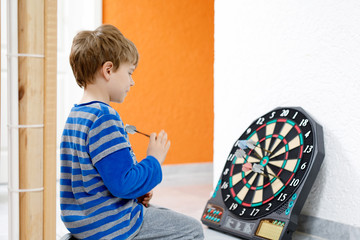 Little cute blond preschool kid boy playing dart, indoors.
