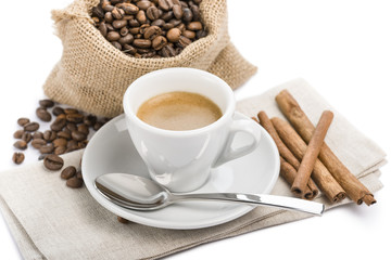 cup of coffee on napkin with canvas bag full of coffee beans and cinnamon, on white background