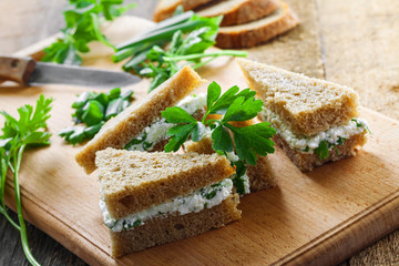 Small sandwiches made of rye bread, cream cheese, fresh parsley and green onion on a table. Simple homemade snack.
