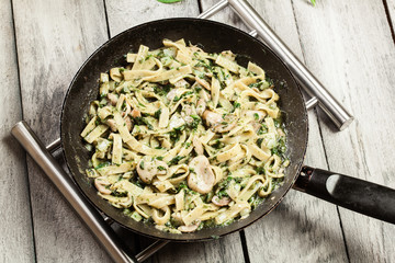 Tagliatelle pasta with spinach and mushrooms on a pan.