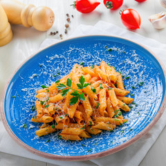 Tasty Italian penne pasta with tomato sauce on a blue rustic plate. Delicious healthy Italian food on a white wooden table. Top view.