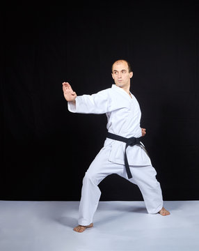 On a black background, an athlete in karategi trains a block with his hand
