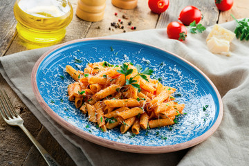 Traditional penne pasta with hot arrabiata tomato sauce and parsley on a rustic wooden table. Traditional Italian healthy food on a blue plate. Top view.