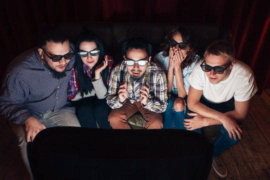 Young people in 3d glasses watch tv on couch. Five friends amazed by exciting effects of new technologies.