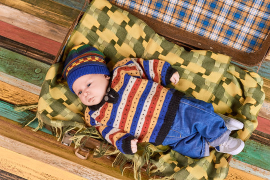 Baby in sweater and hat. Suitcase with kid, wooden background.