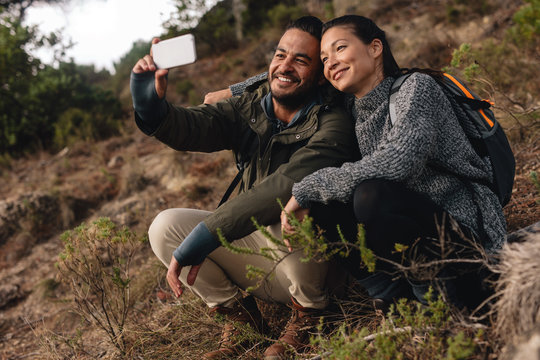 Couple in love sitting on mountain trail and taking selfie