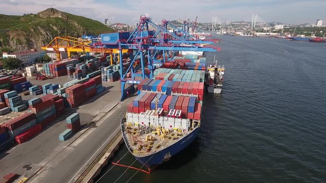 Сontainer ship Free port Vladivostok Russia. Local industrial cranes transport heavy. Golden horn bridge city panorama Steel constructions Port unloading Freight. Summer. Unique Aerial flight around