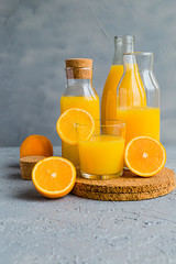 Fresh Orange Juice in Glass and Bottles and some Ripe Oranges on Grey Background. Healthy Drink, diet or Detox. © shutnica