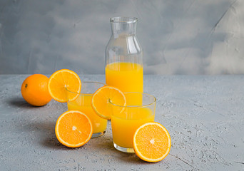 Fresh Orange Juice in Glass and Bottles and some Ripe Oranges on Grey Background. Healthy Drink, diet or Detox. © shutnica