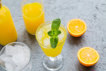 Fresh Orange Juice in Glass and Bottles and some Ripe Oranges on Grey Background. Healthy Drink, diet or Detox.