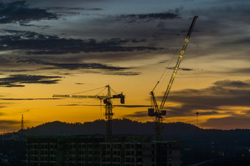 Silhouette of a crane on top of building under construction during sunset