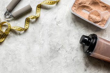 nutrition for workout with protein cocktail powder, measure tape and bars on stone background top view mockup