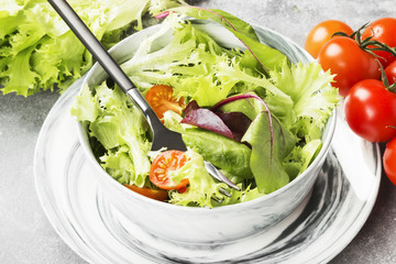 The dietary mixed greens salad (mesclun, mache, lettuce) and cherry tomatoes in a bowl on a light background