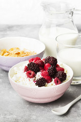 Cottage cheese in bowl with frozen raspberry and blackberry and milk in glass on a light background