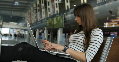 Pretty young female passenger making online shopping using credit card on laptop while waiting on the international airport