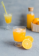 Fresh Orange Juice in Glass and Bottles and some Ripe Oranges on Grey Background. Healthy Drink, diet or Detox.