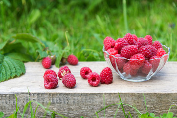 red raspberries in bowl on wooden and grass background