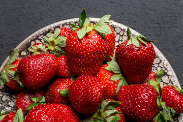 fresh ripe useful fruit strawberry in a clay bowl closeup on a black background